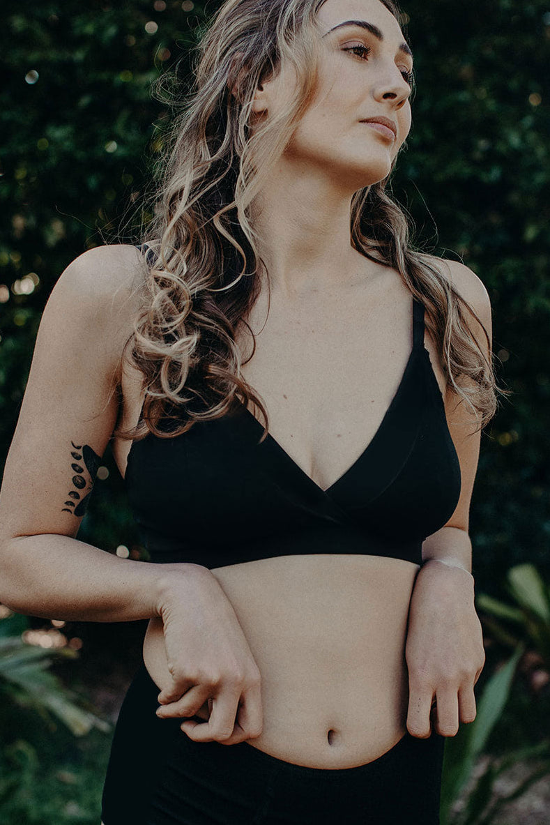 Woman wearing a black cotton bra standing outdoors with greenery in the background