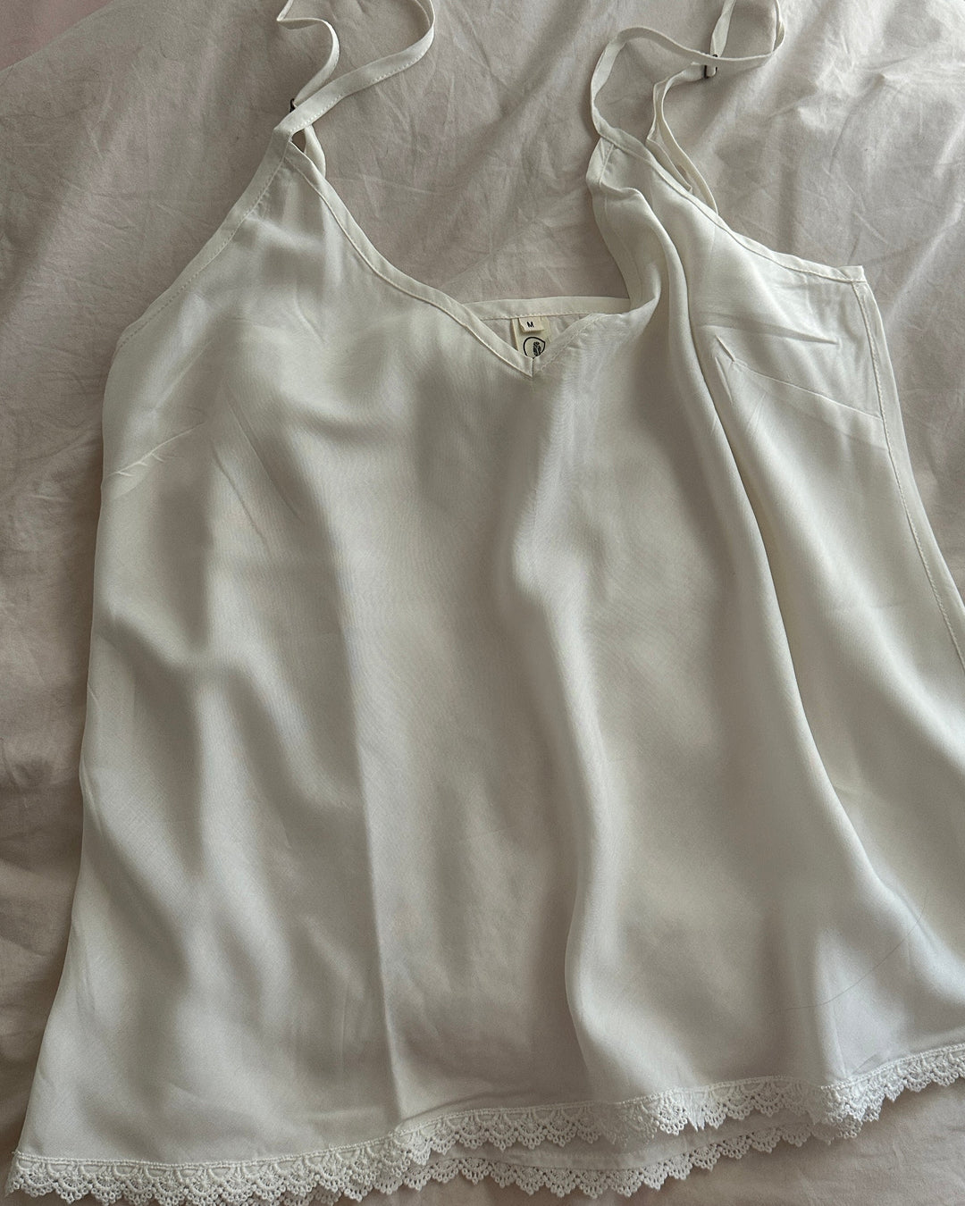 White lace-trimmed camisole on a light-colored fabric background