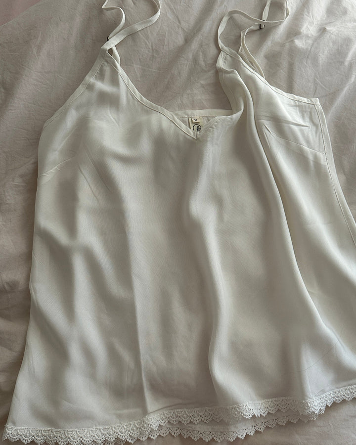 White lace-trimmed camisole on a light-colored fabric background