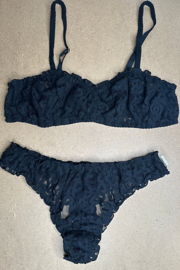 Black lace lingerie set on a cardboard surface with a patterned fabric background.
