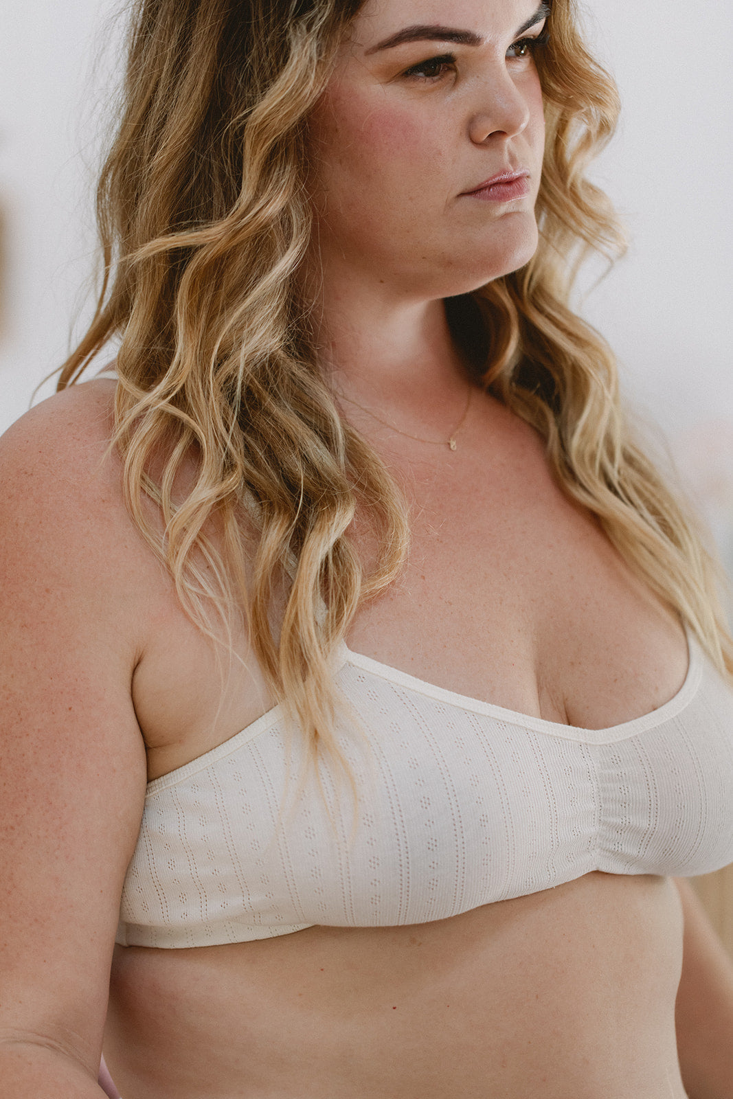 Woman wearing a white organic cotton bralette against a plain background