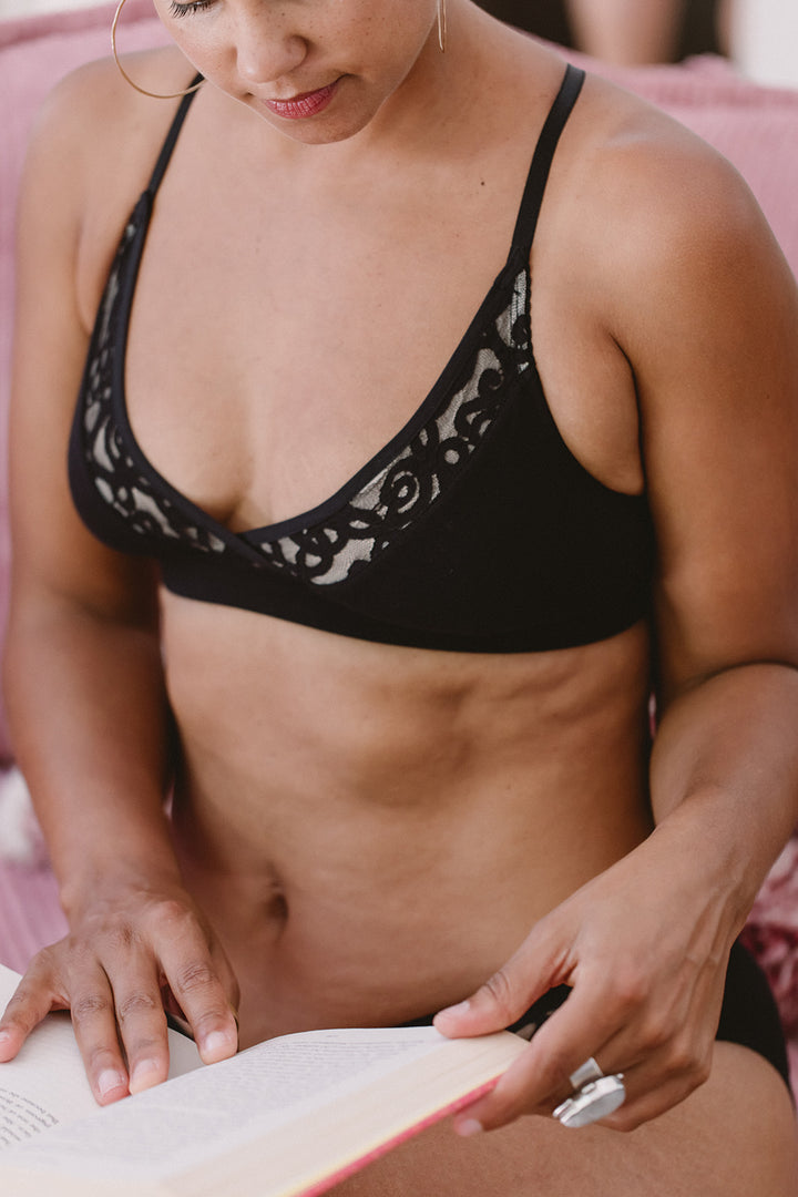 Woman wearing a black lace bralette holding a book.
