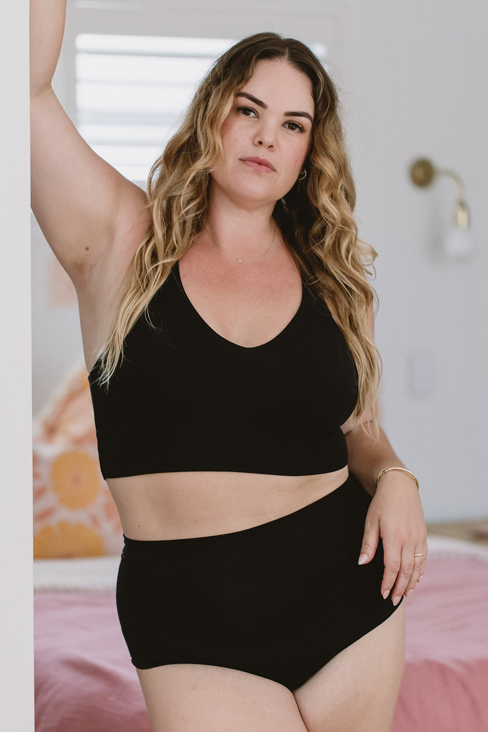 Woman wearing a black sports bra and high-waisted shorts in a bedroom setting.