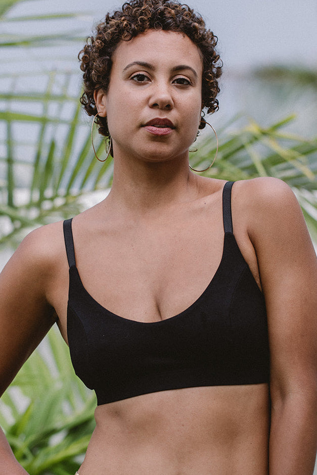 Woman wearing a black underwear standing in front of green foliage