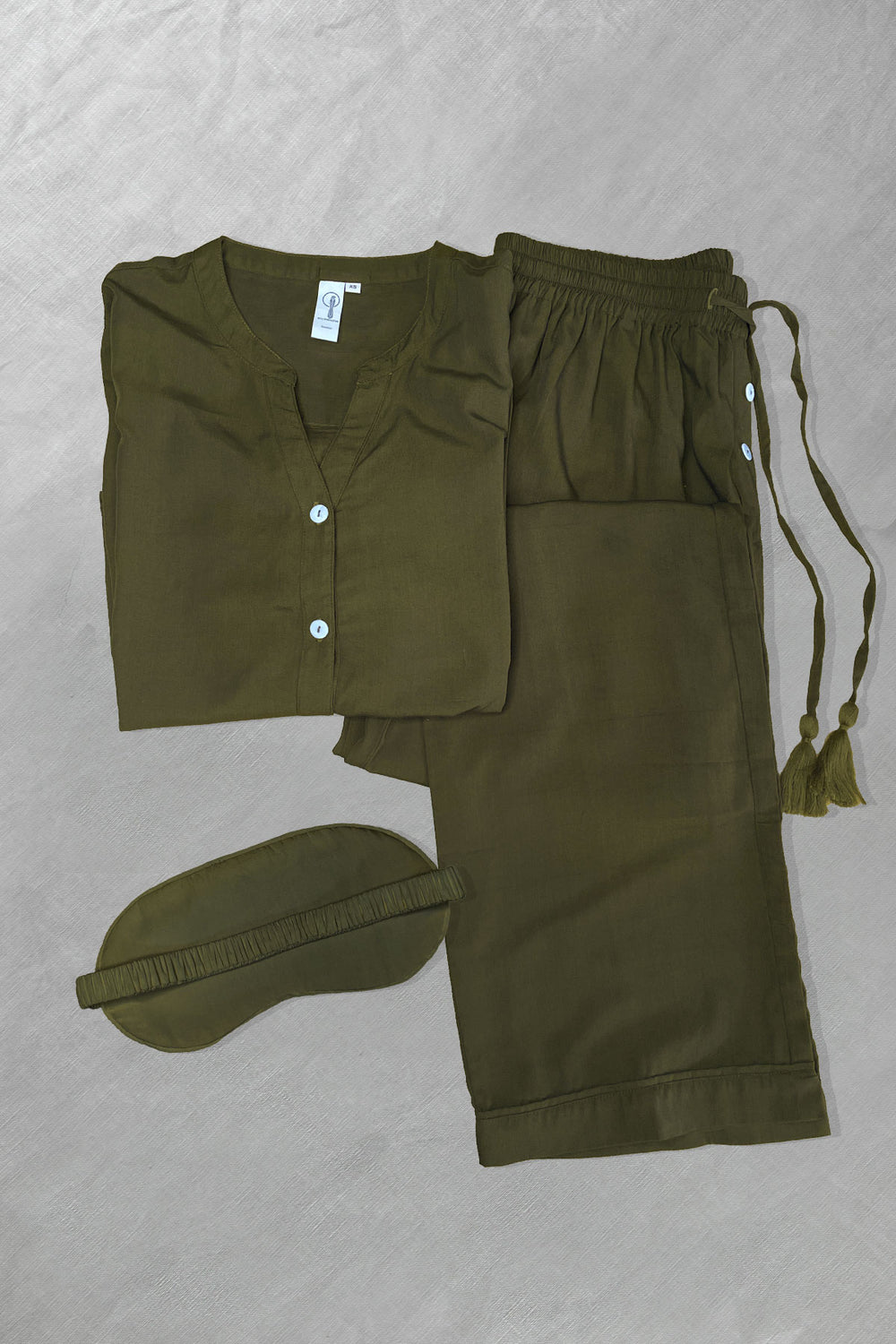 An olive green long sleeve shirt, pants, and a sleep mask with a drawstring and tassel, all laid out flat.
