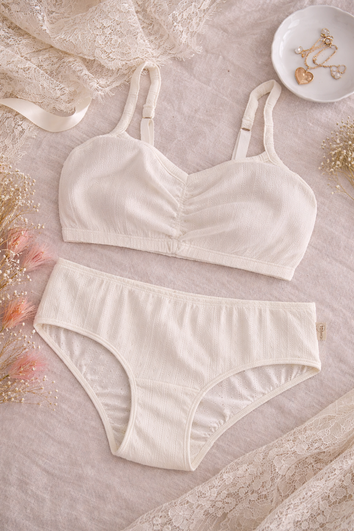 Set of cream-colored bra and panties on a textured surface with decorative elements.