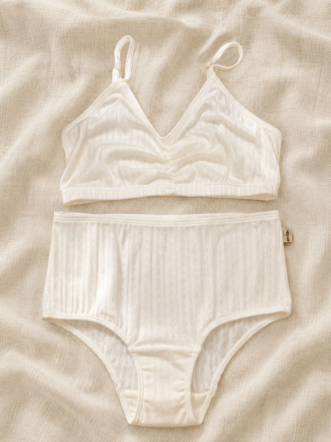 White cotton lingerie set on a beige fabric background, off white cotton underwear in pointelle 