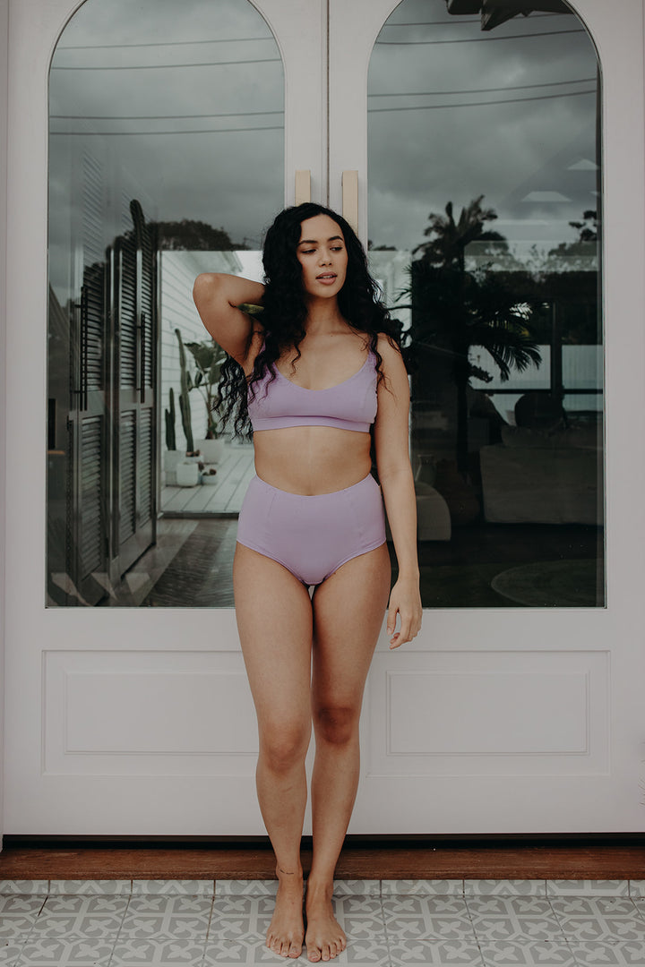 woman standing in front of glass doors, wearing lavender underwear in organic cotton