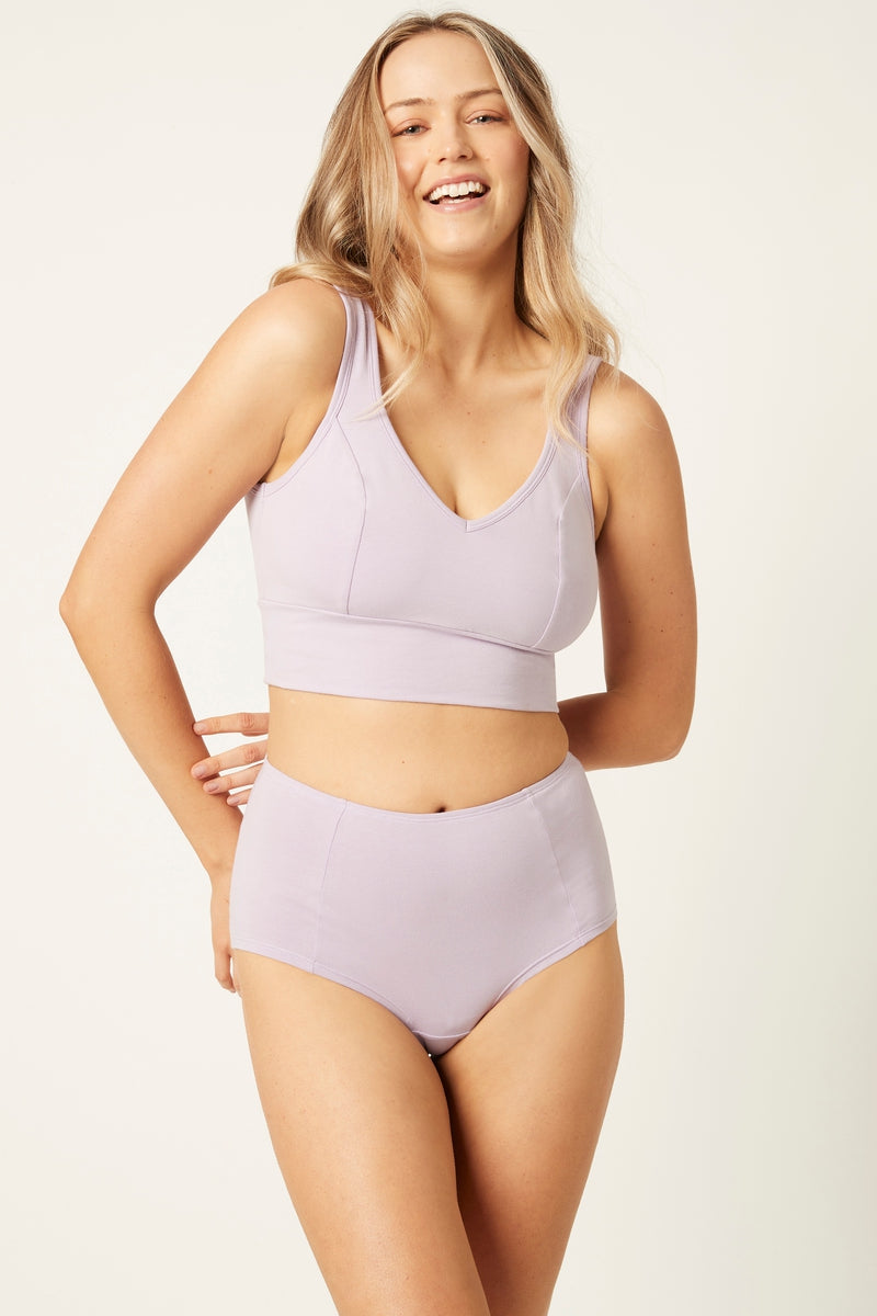 A woman wearing a lavender full cup crop top and matching high-waisted briefs.